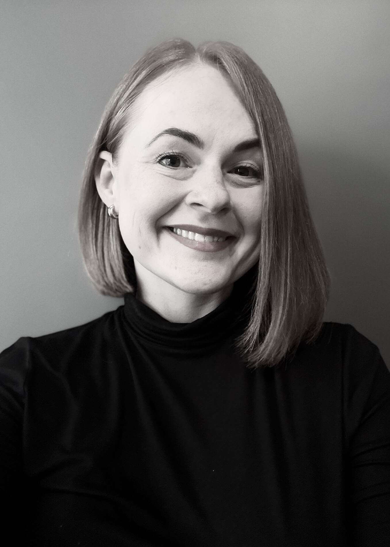 Czarno-biały portret uśmiechniętej kobiety w ciemnym golfie - Natalii Bartoszewicz - Architekt w Białymstoku.